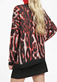 Černý a červený vzorovaný svetr s volným střihem, měkkou texturou, dlouhými rukávy a zakulaceným lemem, kombinovaný s černou sukní.