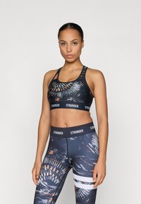 Sutiã desportivo e leggins de cintura alta em tecido escuro com padrões abstratos coloridos. Apresenta uma faixa com o logótipo e várias riscas nas leggins.