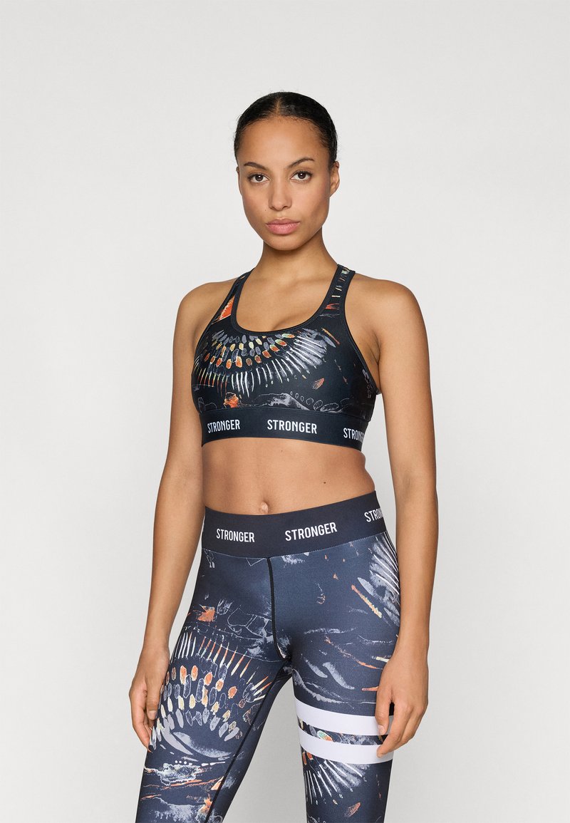 Sutiã desportivo e leggins de cintura alta em tecido escuro com padrões abstratos coloridos. Apresenta uma faixa com o logótipo e várias riscas nas leggins.