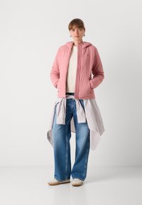 Lichtroze geborduurde jas met een capuchon, gecombineerd met een crèmekleurige trui en blauwe wijde jeans, aangevuld met een gestreept shirt dat om de taille is geknoopt.