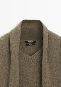 Gebreid vest in een gedempte bruine kleur, gemaakt van 100% wol. Heeft een V-hals en sjawlkraag, met een zachte, gestructureerde afwerking.