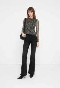 Black flared jeans paired with a long-sleeve top featuring a sheer, zebra-print design. Model holds a black shoulder bag.