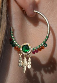 Boucle d'oreille en or avec des perles vertes et rouges, présentant un grand bijou vert au centre, et trois accents en métal en forme de plume suspendus.
