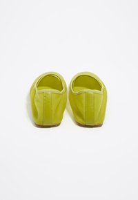 Zelené slip-on topánky v limetkovej farbe so hladkým povrchom, zaoblenou špičkou a minimálnymi švami. Majú mäkké vnútorné podšívku a plochú hnedú podrážku.
