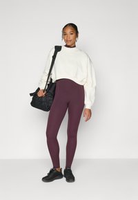 Kremfarget kort genser, burgunder høyhøydede leggings, svarte joggesko, svart veske med justerbar stropp, glatte teksturer og enkelt design.
