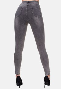 Jeans gris ajustados con cintura alta, bolsillos traseros y una textura ligeramente desgastada. Combinados con zapatos de tacón negros.