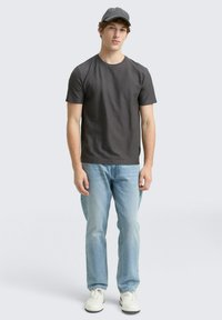 Tricou scurt de culoare gri închis, purtat cu blugi albaștri deschis și adidași albi. Echipat cu o șapcă gri închis asortată. Design simplu și modern.