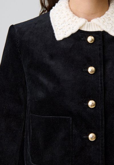 Giacca in velluto a coste nera con colletto crema testurizzato e dettagli in perle. Bottoni dorati e tasca a soffietto arricchiscono il design.