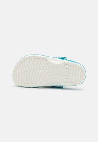 Bílá podrážka boty ve stylu dřeváků s texturovaným dezénem; svršek má modro-turquoise vzorovaný design.