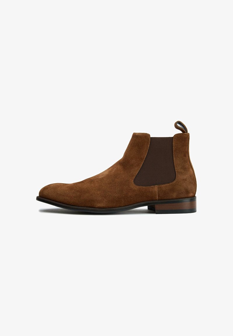 Suede brown Chelsea boot featuring elastic side panels, a rounded toe, a small heel, and a loop for easy wear. Smooth texture throughout.