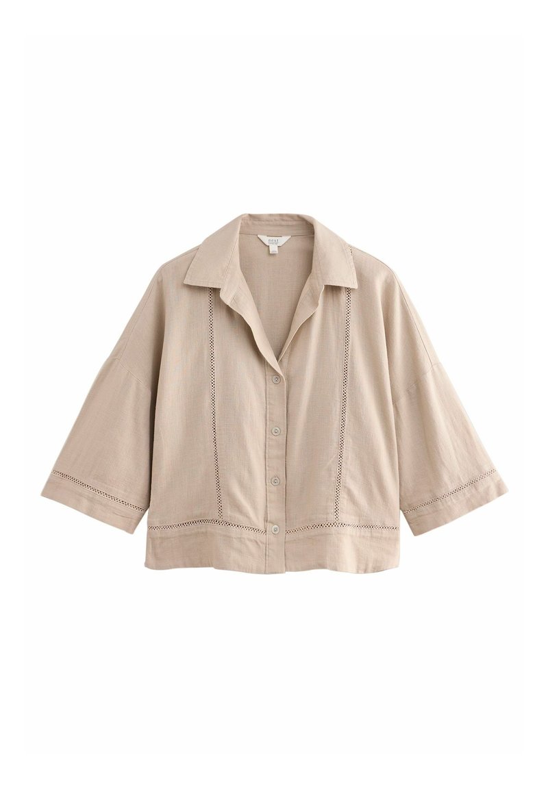 Chemise beige à manches courtes avec boutons, col large et motifs décoratifs de coutures verticales et horizontales sur le devant et les manches.