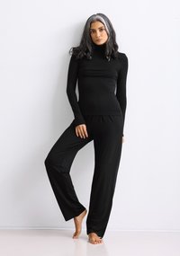 Black long-sleeve top with a high collar, paired with loose-fitting black pants. Smooth, stretchy fabric with a sleek, minimalist design.