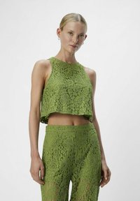 Un top corto de encaje verde y pantalones a juego presentan patrones florales, un escote alto y un ajuste holgado, exhibiendo texturas intrincadas y recortes.