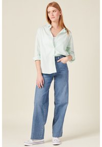 Camicia a righe verde chiaro, taglio rilassato, maniche arrotolate, abbinata a jeans a gamba larga in denim blu a vita alta e sneakers bianche.