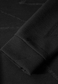 Schwarzer Strickstoff mit einem strukturierten Muster und dezenten glänzenden Akzenten. Nahaufnahme eines gefalteten Ärmels mit Rippbündchen.