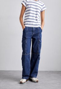 Pantalones cargo de mezclilla en azul oscuro con múltiples bolsillos, diseño de pierna recta y costuras en contraste. Combinados con una blusa de rayas de manga corta.
