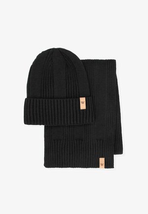 Schwarzes, geripptes Strick-Beanie und passendes Schal-Set. Beide Teile sind mit einem Lederetikett mit dem Buchstaben "W" versehen. Glatte Textur, einheitliche Farbe.