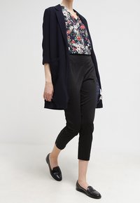 Marine lang jakke, bluse med blomsterprint, sorte tætsiddende bukser og sorte loafers. Bløde stoffer, skræddersyet pasform og trekvartlange ærmer.