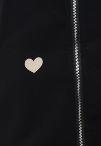 Μαύρο ύφασμα με σχέδιο σε σχήμα καρδιάς σε ανοιχτό μπεζ χρώμα και ασημί φερμουάρ στη δεξιά πλευρά. Λείο υλικό, κοντινή λήψη.
