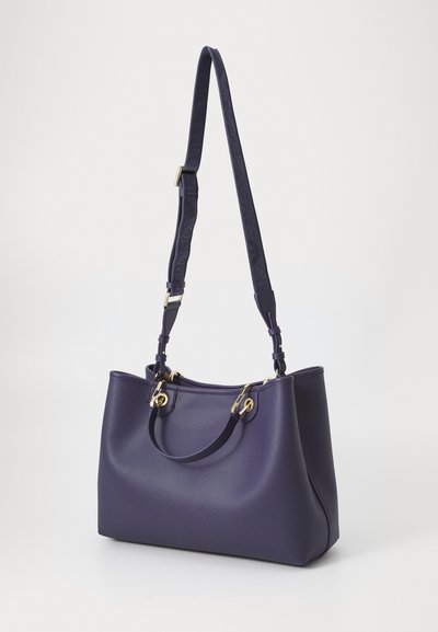 Deep purple handbag with a structured shape, features gold hardware, dual handles, and an adjustable strap, set against a white background.