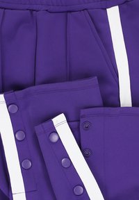 Paarse sportbroek met witte zijkanten en drukknoopjes langs de buitenste naden, met een close-up van de tailleband en de broekopeningen.