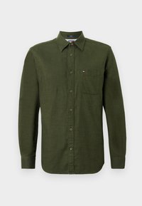 Πράσινο πουκάμισο με κουμπιά και μακριά μανίκια, κατασκευασμένο από υφασμάτινο υλικό. Διαθέτει μια τσέπη στο στήθος και ένα μικρό λογότυπο στην περιοχή του στήθους.