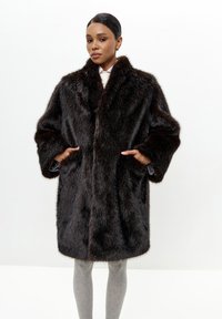 Brun kunstpelsjakke med en bred krave, oversized pasform og store lommer, med en glat inderside og en tekstureret yderside.