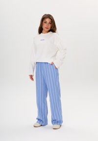 White long-sleeve shirt with blue text, paired with light blue striped wide-leg pants. The outfit features soft fabric and relaxed fit.