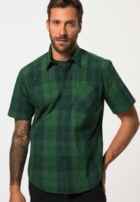 Camisa corta de manga corta de cuadros verdes hecha de algodón. Tiene un frente con botones, un bolsillo en el pecho y patrones de cuadros en verde oscuro que contrastan.