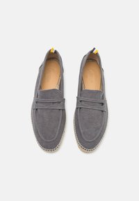 Grå lærredssko med slip-on design, der har et dekorativt bånd og beige syninger, flad, flettet jute sål og en gul hælaccents.