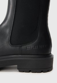 Cizma din piele neagră cu panou elastic pe lateral și logo-ul gravat "REPLAY MFG CO" pe toc, deasupra unei tălpi groase din cauciuc.
