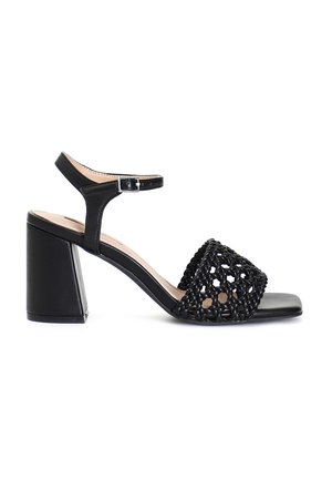 Sandal con tacco nero caratterizzato da una tomaia intrecciata, punta aperta e cinturino alla caviglia regolabile. Il tacco a blocco offre stabilità e altezza.