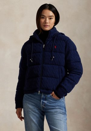 Chaqueta de punto trenzado de color azul marino con cremallera, que incluye capucha, puños y dobladillo acanalados, con cordones y un pequeño logo rojo en el pecho.