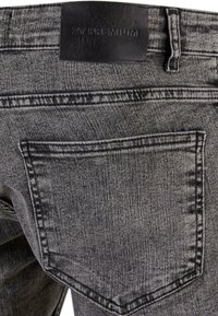 Pelēki denim džinsi ar teksturētu apdari, kas aprīkoti ar aizmugurējo kabatu un melnu ādas etiķeti ar uzspiesto uzrakstu "2Y PREMIUM" jostasvietā.
