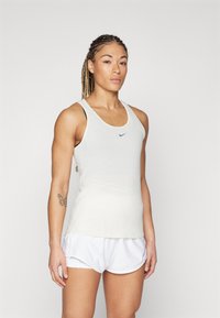 Débardeur de sport blanc avec un logo bleu, associé à un short blanc. Le tissu semble léger et lisse, offrant une coupe ajustée.