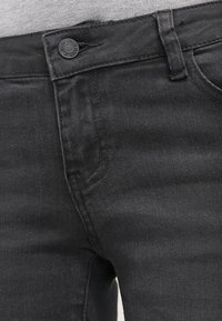 Vaqueros de mezclilla negros con una textura suave, diseño de cinco bolsillos y cierre frontal con botón. La tela tiene un aspecto ligeramente desgastado.