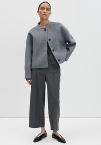 Veste courte en mélange de laine gris avec un col montant, des boutons sur le devant et des manches larges, associée à un pantalon gris ajusté et des ballerines noires.