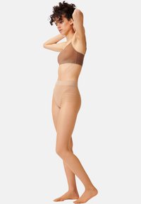 Bralette marrone con una sottile tracolla e una fascia ampia, abbinata a leggings trasparenti color sabbia a vita alta con sottili accenti a coste.