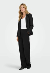 Zwarte op maat gemaakte blazer met een enkele knoop, gecombineerd met brede zwarte pantalons en een witte getailleerde tanktop; gladde stof en minimalistisch ontwerp.