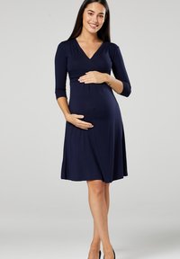 Navy blue maternity dress with three-quarter sleeves, V-neckline, and gathered fabric under the bust, creating a flowing silhouette.