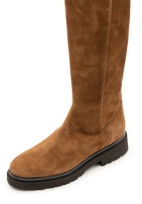 Brauner kniehoher Wildlederstiefel mit abgerundetem Zehenbereich, glatter Textur und dicker schwarzer Gummisohle. Schlichtes Design mit minimalen Nahtdetails.