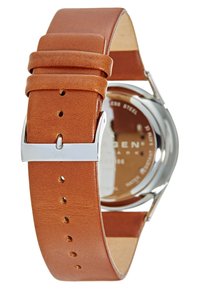 Cinturino in pelle marrone con fibbia in metallo argentato, che mostra una cassa rotonda in acciaio inossidabile e un retro in vetro trasparente che espone il meccanismo dell'orologio.