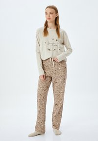 Lange mouw lichtbeige top met sterrenprint en bruine broek met een patroon van hemelse ontwerpen in wit en beige tinten. Zachte stof, casual pasvorm.