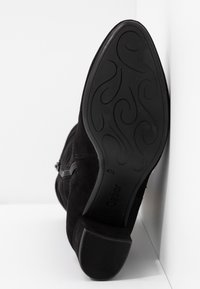 Bottine en daim noir avec un petit talon, dotée d'une semelle en caoutchouc texturée et d'une fermeture éclair latérale pour un enfilage facile. Taille indiquée : 4,5.