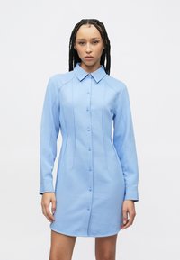 Blauwe jurk met lange mouwen, een kraag en een knoopsluiting aan de voorkant. Gladde stof met naaddetails langs de zijkanten.