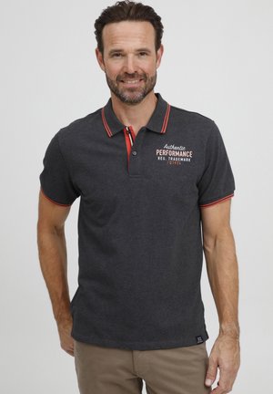 Polo de color gris oscuro con detalles rojos en el cuello y las mangas. Presenta un estampado frontal con texto. Confeccionado en un tejido suave, diseño de manga corta.