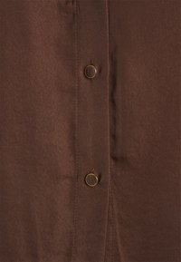 Brun skjorta med knapp-up som har en slät, lätt glänsande yta, två runda knappar och en skräddarsydd passform.