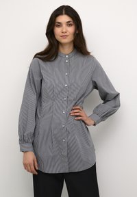 Camicia a righe con bottoni, tessuto leggero, colletto, maniche lunghe con polsini abbottonati, patta centrale con bottoni, righe verticali nere e bianche.