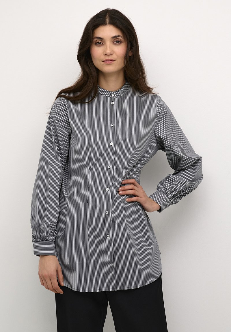 Camicia a righe con bottoni, tessuto leggero, colletto, maniche lunghe con polsini abbottonati, patta centrale con bottoni, righe verticali nere e bianche.