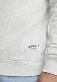 Light grey sweatshirt made of soft fabric with ribbed cuffs and hem. Features a white label with blue text on the left side.